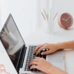 Hands typing on a laptop at a clean minimal desk