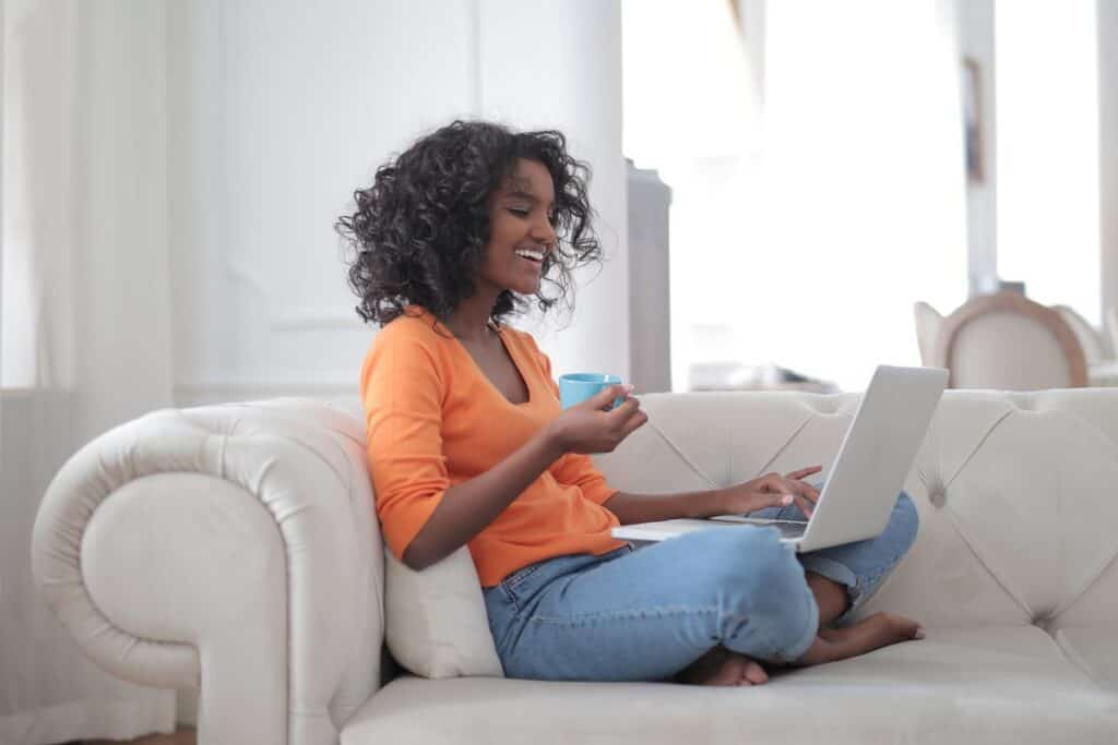 Woman working on a laptop on a bright couch with coffee