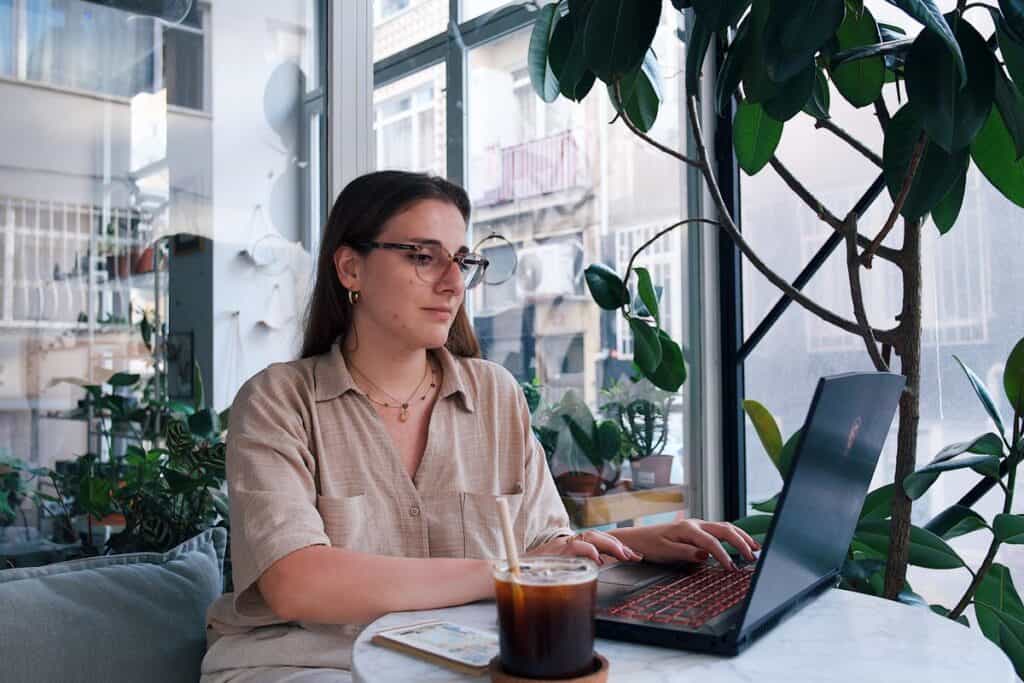 Woman working on a laptop in a plant-filled cafe