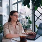 Woman working on a laptop in a plant-filled cafe