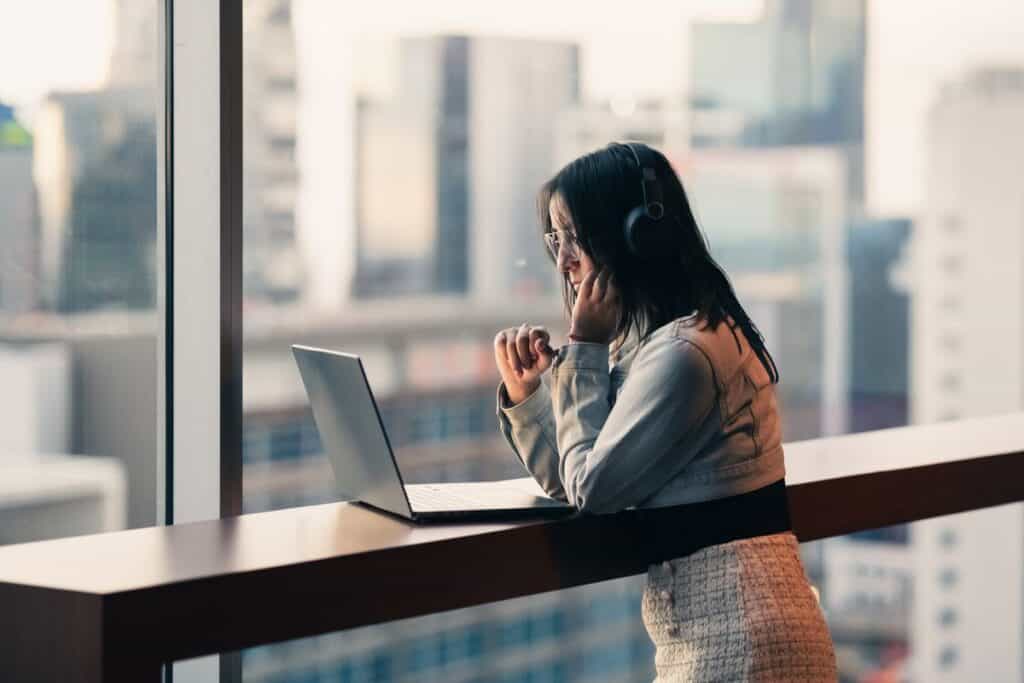 Woman working on a laptop by a window with city view