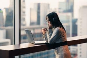 Woman working on a laptop by a window with city view